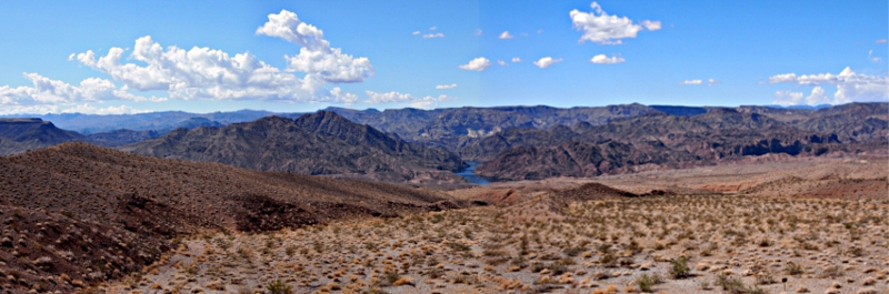 [Zoomed out photo of the prior one showing more of the sky and the puffy white clouds and the surrounding rocky, desert terrain.]